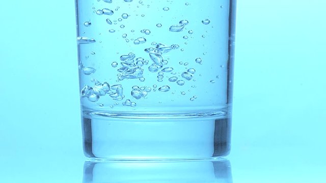 Glass of Sparkling Water against Blue Background, Slow Motion