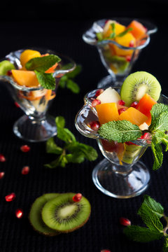 Fruit desserts, salad of pineapple, papaya, pomegranate and mint, kiwi on a dark background