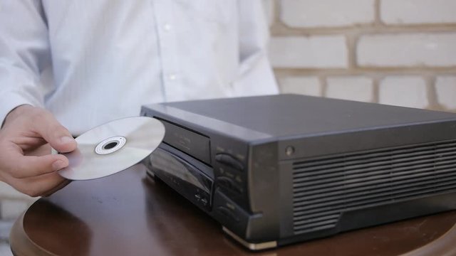 The man trying to load DVD disc to old video cassette VHS recorder. The difficulty with the replacement of the VHS to DVD.