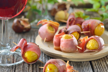 Gebackene Maroni im Südtiroler Speck als Fingerfood zum Törggelen mit regionalem Wein gereicht - Roasted chestnuts wrapped in South Tyrolean bacon served on skewers with local red wine