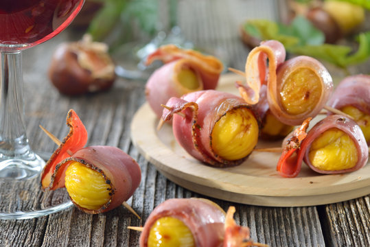Gebackene Maroni im S&uuml;dtiroler Speck als Fingerfood zum T&ouml;rggelen mit regionalem Wein gereicht - Roasted chestnuts wrapped in South Tyrolean bacon served on skewers with local red wine