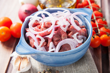 the meat cut by pieces with onions in a bowl on a table, ingredients for beef Stroganoff, selective focus