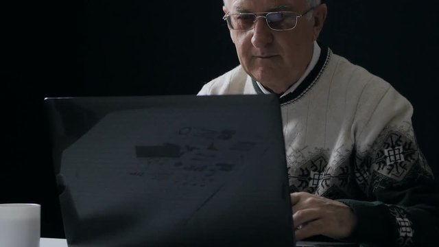 Senior man working at a laptop in dark room