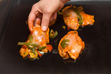 Women's hand put chicken in curry sauce with peppers on the pan to broil in the oven. Daily food.