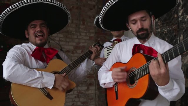 Mexican musician playing guitar and accordion in the studio, in the interior. Men are smiling.