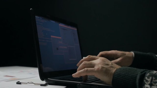 Senior man working at a laptop in dark room