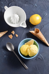 Lemon ice cream bowl, cones and lemon on the dark blue surface.