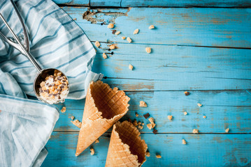 Traditional waffle cones for ice cream and a spoon for it on blue wooden table. Summer, open space, bright sun Wafers and chocolate chips in a frame on the table. One of cones filled with ice cream