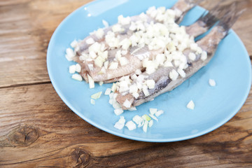 Traditional Dutch raw herring with onions on plate on wooden background
