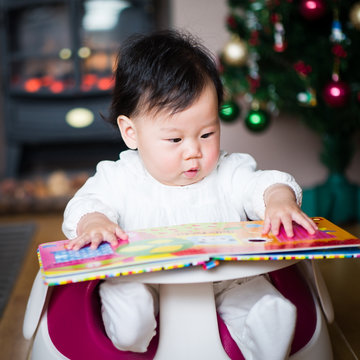 Asian baby girl reading book against Christmas tree background