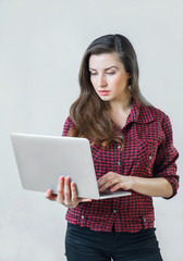 Fototapeta premium Young girl looks at the screen silver notebook silver and typing with one hand