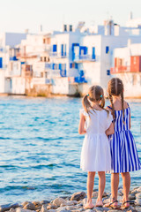 Fototapeta na wymiar Little kids at Little Venice the most popular tourist area on Mykonos island, Greece. Back view of beautiful girls look at Little Venice background.