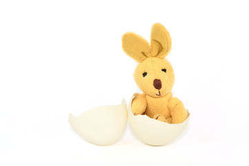 Little brown Plush Rabbit seated inside of a half egg and another half beside
