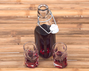 Homemade raspberry liqueur in clear glass bottle with swing top and shot glass on bamboo table