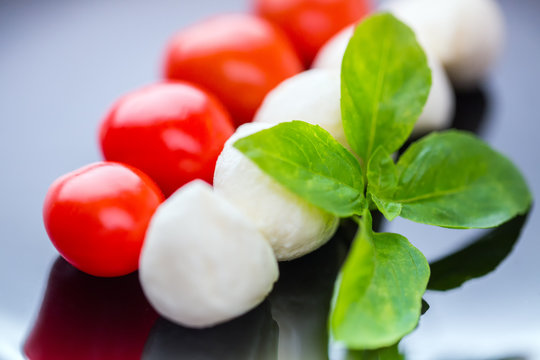 Italian salad. Cheese mozzarella, basil and tomatoes on a fork on a black plate. In small DOF.