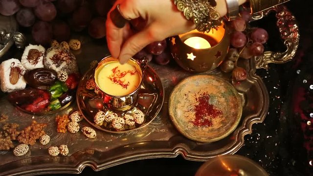 Female hands with beautiful oriental accessories Making Saffron Masala milk Tea with indian spices. Traditional Moroccan Sweets. Gala dinner by candlelight. Arab, Turkish, Persian and Indian dishes
