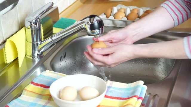 Woman hands washing fresh egg in kitchen under water stream. Wash eggs before eating. Protect health 4K ProRes HQ codec