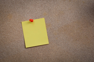 Blank yellow paper note pinned on cork board with white thumbtac