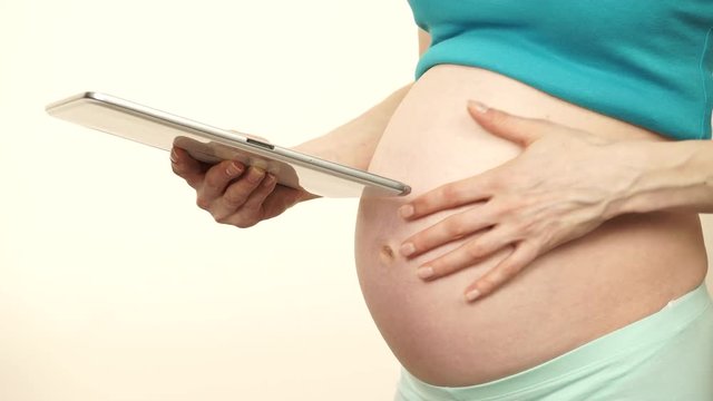 Pregnant woman no face touching her naked big belly while using smart phone, reading message. Studio shot on white. Pregnancy, motherhood, baby anticipation and technology concept. 4K ProRes HQ codec
