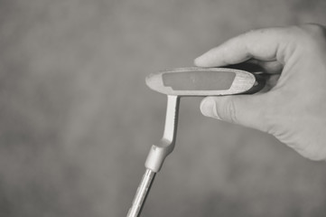 Black white closeup of a golfers hand using golf club, grass background