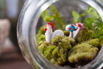 A terrarium garden scene in glass ball shape with Tillandsia, pebbles and flamingo toy inside and...