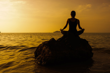 Silhouette of woman practicing yoga on the beach during a beauti