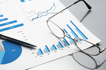Blue charts, glasses and pen. Financial report on gray reflection background.

