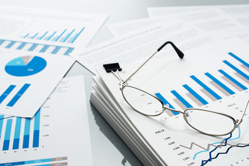 Checking business reports. Glasses and pile of documents. Many graphs and charts. Pile of documents on gray reflection background.
