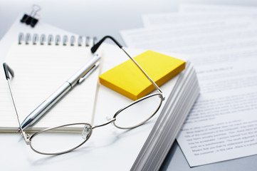 Checking and reviewing documents. Glasses, pen and pile of documents.
Pile of documents on gray reflection background.
