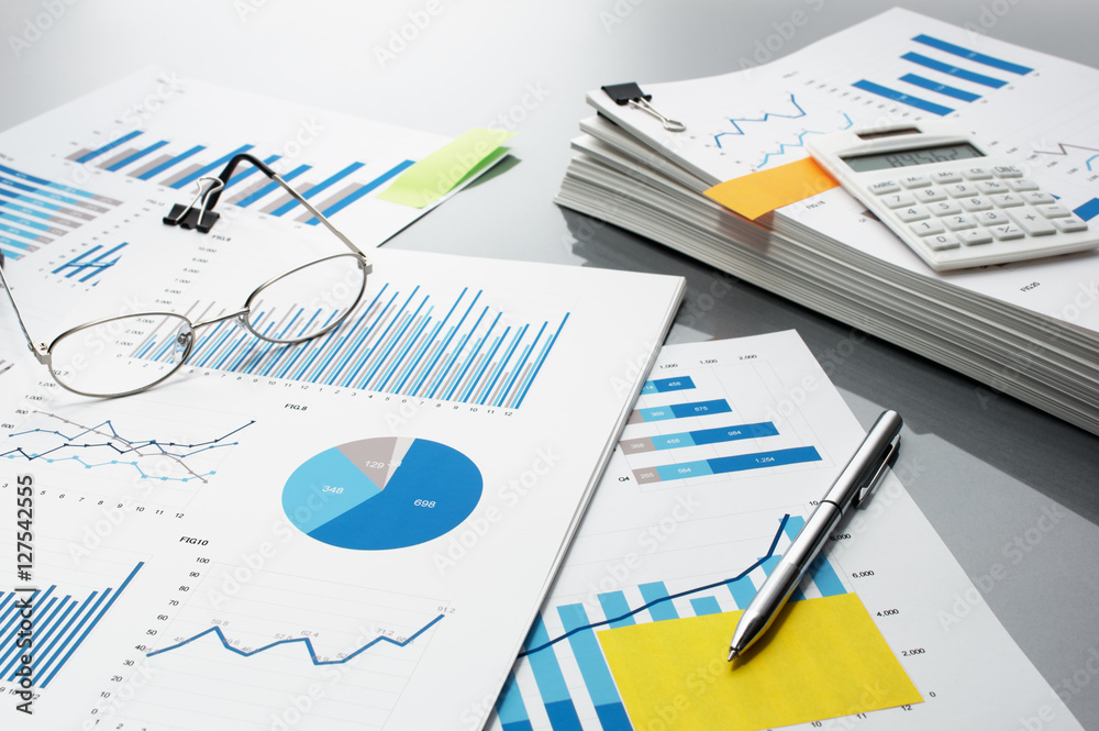 Poster preparing report. blue graphs, glasses, calculator and pen.　business reports and pile of documents o