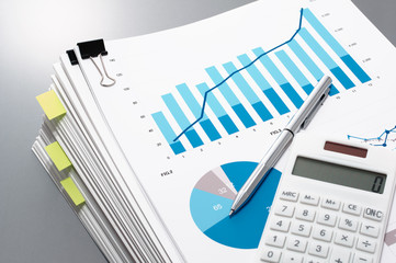 Pile of documents, calculator and pen on gray reflection background.
Reviewing report. Many graphs and charts.
