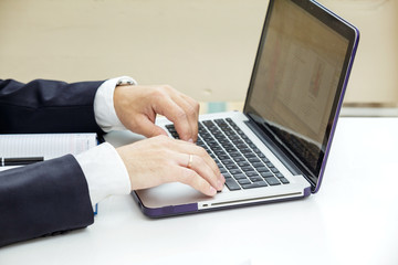 Businessman typing on a laptop. The man in a suit and a white shirt. Closeup.