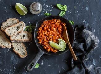 Braised beans in tomato sauce in a cast iron pan and homemade bread on wooden cutting board.