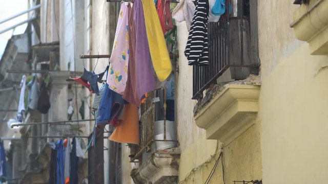 View to old balcony on a colonial Havana street where the multi-colored clean wet washed clothes of local people are drying at summer sunny day