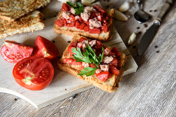 tomato and tuna bruschetta on rustic, old wood background. top view