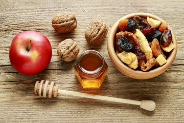 Bowl of dried fruits, red apple, nuts and jar of honey on wood