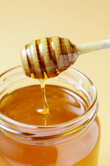 Fototapeta na wymiar Honey spoon over the big jar full of golden liquid
