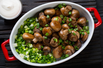 Bowl with whole fried champignons and green onion, closeup
