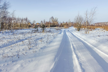 Fototapeta na wymiar Countryside road through winter field with village on a horizon