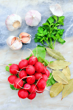 Radishes and garlic on a light background. Beautiful still life of fresh vegetables and bay leaf.