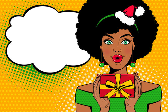Pop art face. Sexy afro american woman with open mouth in Santa Claus hat holding a gift box in her hands and speech bubble. Vector Christmas background in pop art retro comic style. Party invitation.