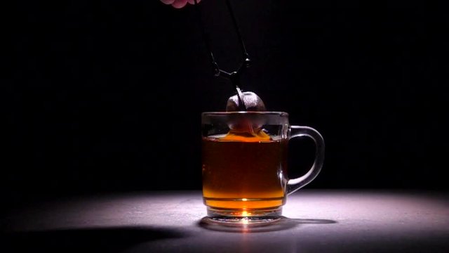 Glass teacup with tea strainer. Slow motion film clip with black background.