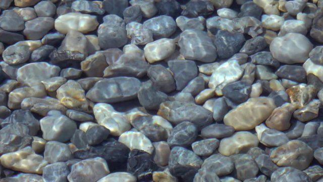Slow motion, 240fps, of abstract natural background. Beautiful view for amazing intro in excellent eight times decelerated clip. Soft ripple on shallow transparent water surface with pebble bottom.