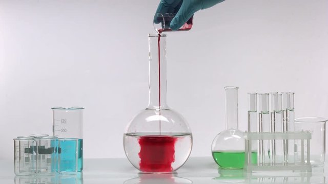 Pouring red solution from beaker into flat-bottomed flask with swirling transparent liquid