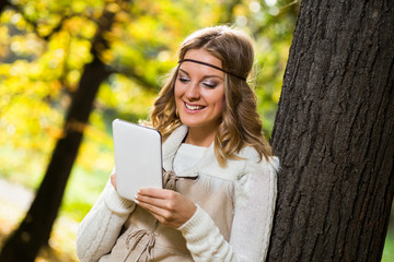 Beautiful boho girl enjoys using digital tablet in the park.