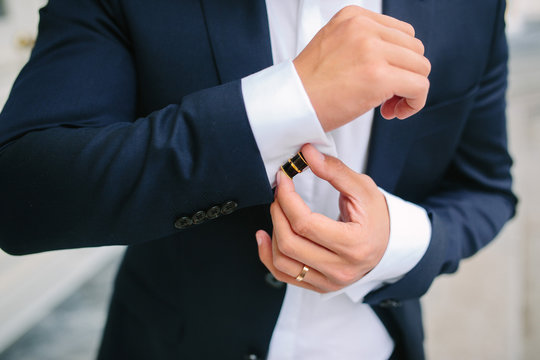 elegant young fashion man looking at his cufflinks while fixing them