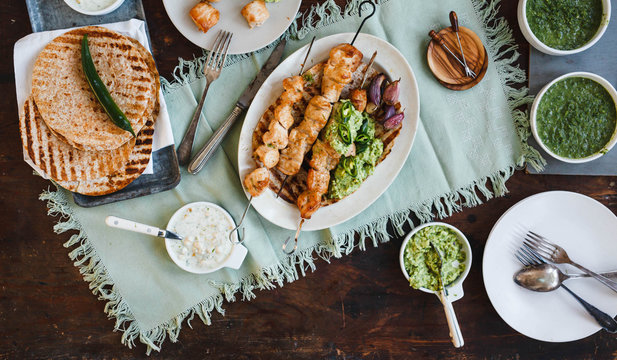 Mexican food table with chicken skewers, avocado cream sauce, and flatbread. 