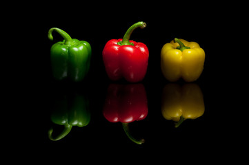 Three whole bell peppers yellow green red isolated on black back