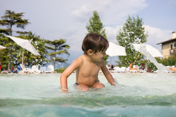Naklejka premium Young boy kid child splashing in swimming pool having fun leisur
