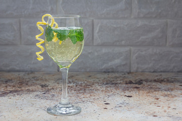 Spritzer cocktail with white wine, mint and ice, decorated with spiral lemon zest, horizontal, copy...